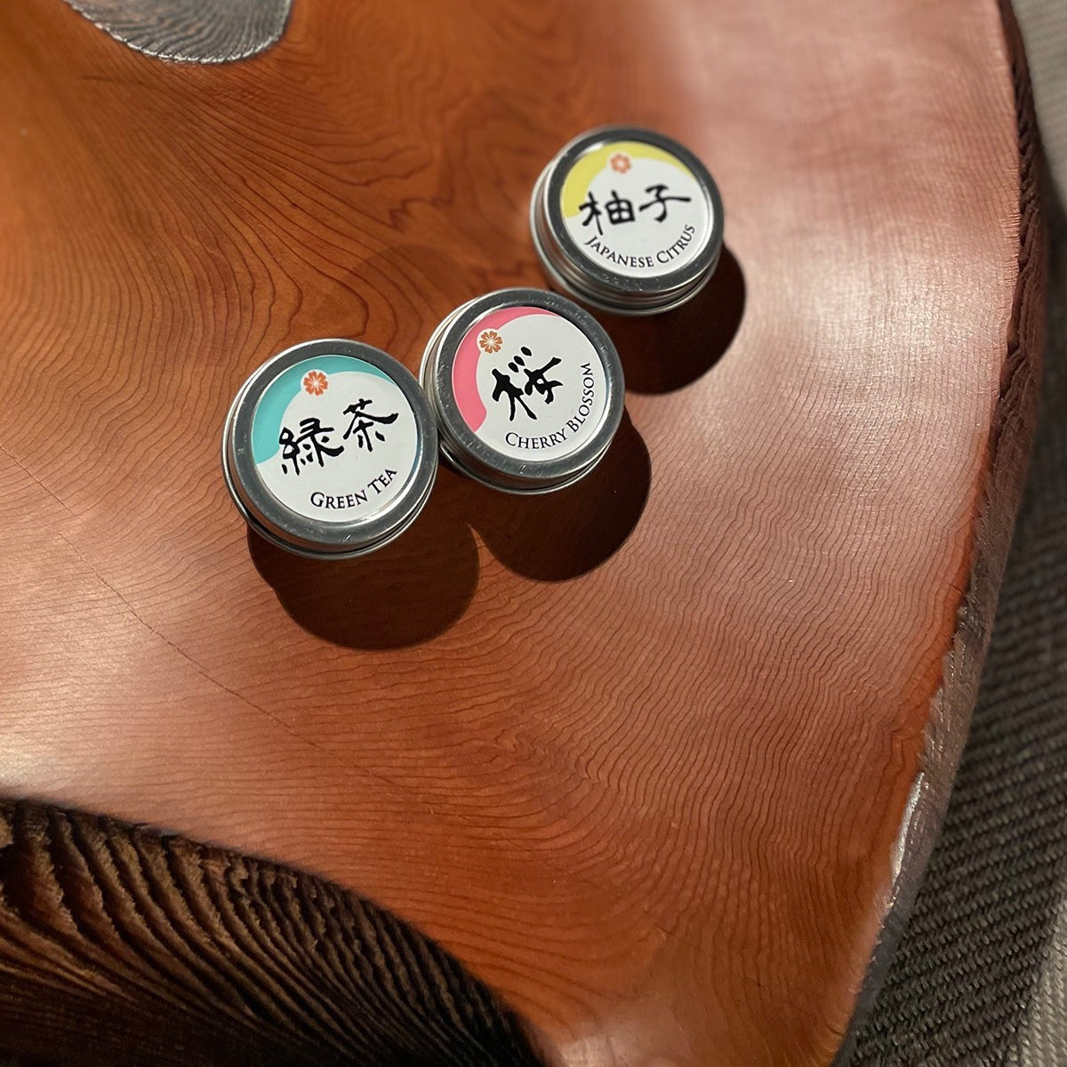 Beauty Secrets of Japan lip balm tins in Green Tea, Cherry Blossom, and Japanese Citrus scents on a wooden surface.